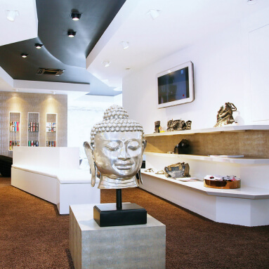 A modern retail store featuring a vintage metal wall panel with a Buddha head sculpture surrounded by colorful products.