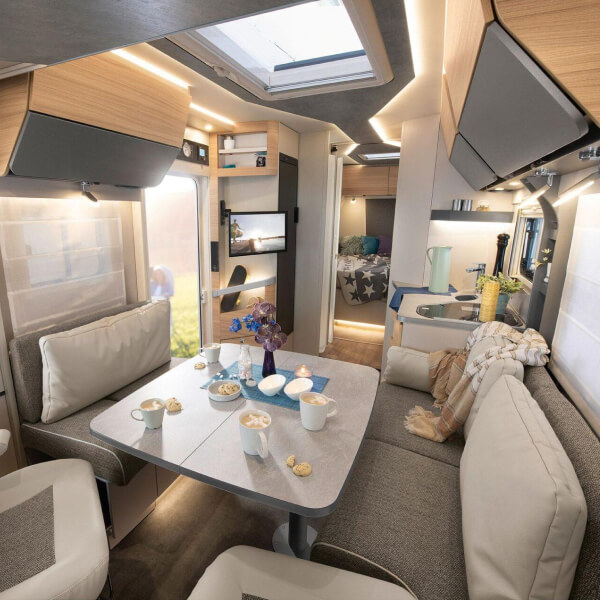 Una sala de estar espaciosa y luminosa en la autocaravana, decorada con un estilo moderno y materiales naturales. Una acogedora zona de estar con una mesa plegable y paneles de madera crea un ambiente cálido y acogedor.