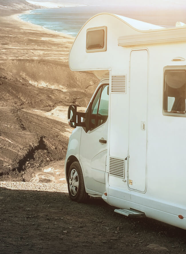 Una autocaravana blanca aparcada en un acantilado con vistas a una carretera sinuosa que conduce a un vasto océano azul.