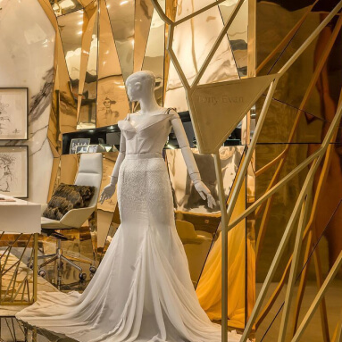 Lujoso salón de novias con un panel de pared de metal espejado que muestra un impresionante vestido de novia en un maniquí.