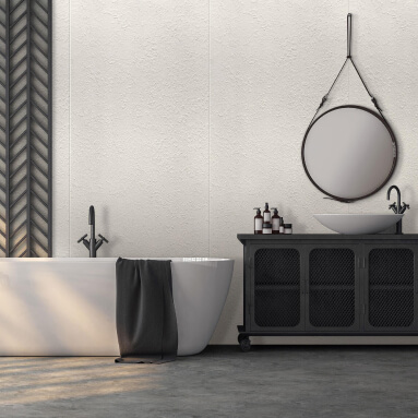 Baño moderno con una bañera ovalada blanca, un mueble bajo lavabo negro y un espejo redondo con marco negro. La pared está revestida con un panel de hormigón texturizado, creando un acento industrial.