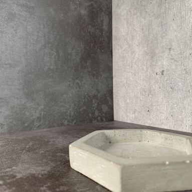 Primer plano de muestras de paneles de pared de hormigón. Se muestran dos tonos de gris con diferentes texturas de superficie. Una pequeña bandeja hexagonal de hormigón se coloca en uno de los paneles.