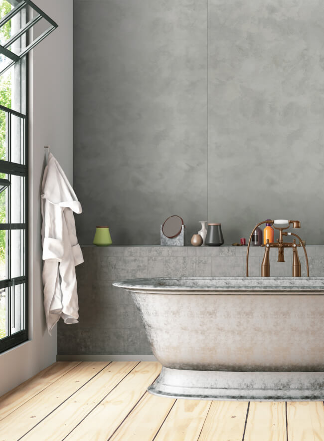 Un baño moderno con un panel de pared de hormigón. Las paredes claras contrastan con la bañera oscura, creando un interior elegante y acogedor. Elementos decorativos y plantas en la estantería añaden vida al espacio. La gran ventana proporciona luz natural.