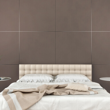 Habitación de hotel moderna con un panel de pared texturizado que imita el cuero en un gris suave. Una cama king-size con sábanas blancas y una manta beige, dos mesitas de noche con lámparas blancas y una pequeña planta en una maceta sobre una alfombra beige.