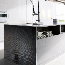 Un panel de pared negro texturizado en una isla de cocina, complementado por un grifo moderno y electrodomésticos de acero inoxidable.