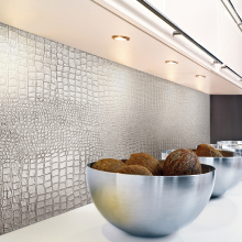 Una cocina con un panel de pared de cuero texturizado de color gris claro con un patrón de piel de cocodrillo. En la encimera frente al panel hay tres cuencos de acero inoxidable llenos de cocos.