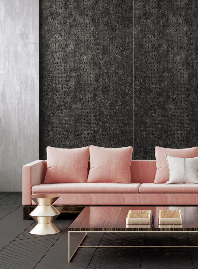 Una sala de estar moderna con un panel de pared de imitación de cuero negro, un sofá rosa y una mesa de centro dorada. La habitación está decorada con un jarrón de flores secas y una pila de libros.