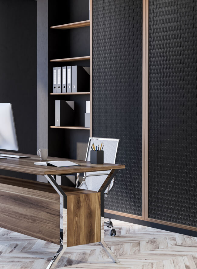 Una oficina moderna con un panel de pared negro con textura tejida, un escritorio de madera, un suelo de parquet claro en espiga y puertas de armario de vidrio.