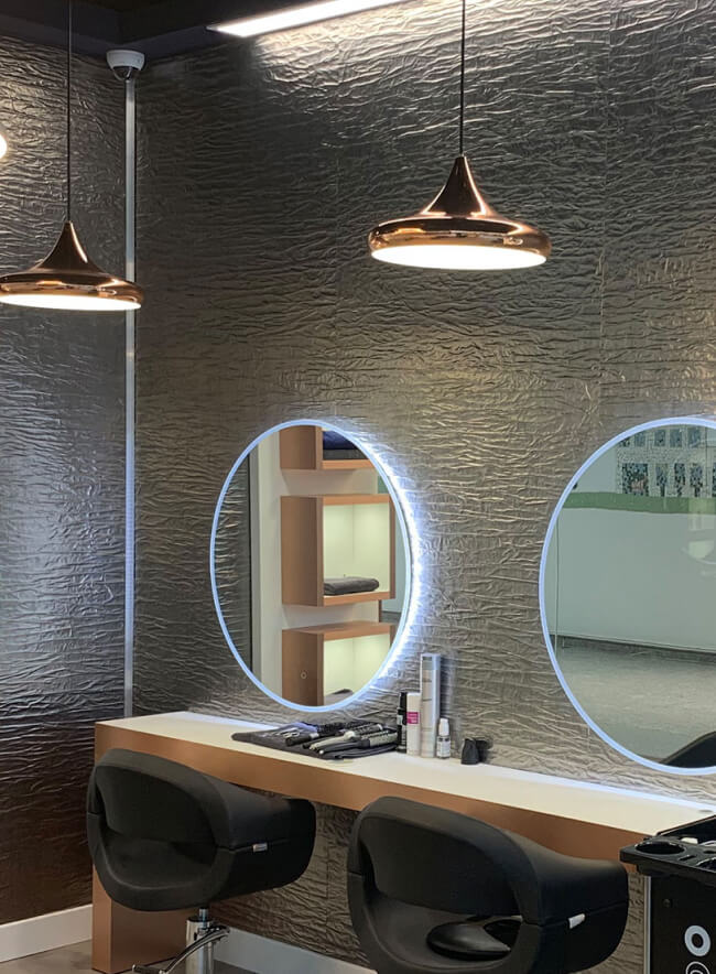 Una peluquería moderna con paneles de pared de metal texturizado 3D. El interior también cuenta con iluminación elegante y cómodas sillas para los clientes.