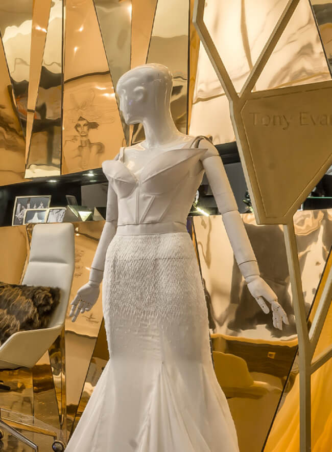 Lujoso salón de novias con un panel de pared de metal espejado que muestra un impresionante vestido de novia en un maniquí.