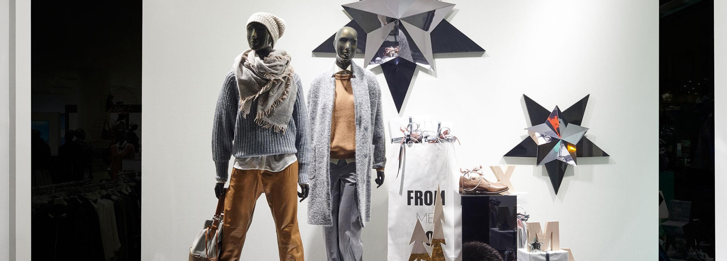 Vitrina de una tienda de moda con dos maniquíes en ropa de invierno. En el centro de atención, un elegante panel de pared de formas geométricas con un brillo metálico. Un diseño interior moderno y elegante que resalta las tendencias de la temporada.