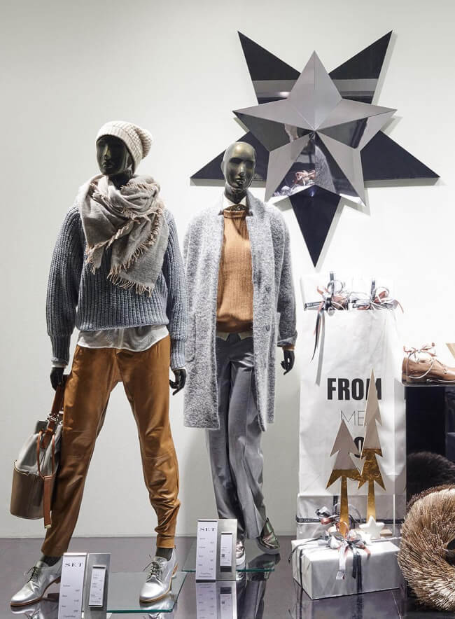 Vitrina de una tienda de moda con dos maniquíes en ropa de invierno. En el centro de atención, un elegante panel de pared de formas geométricas con un brillo metálico. Un diseño interior moderno y elegante que resalta las tendencias de la temporada.