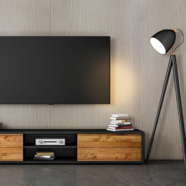 Salón moderno con un televisor de pantalla plana montado en un panel de pared de madera. Debajo del televisor hay un mueble TV de madera con libros y un reproductor de DVD. Junto al televisor hay una lámpara de pie negra.