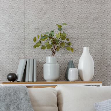 Paneles de pared de cuero texturizados en 3D en la sala de estar, un jarrón con hojas de eucalipto, libros y objetos decorativos en una mesa de centro de madera frente a un sofá blanco con cojines y una manta.