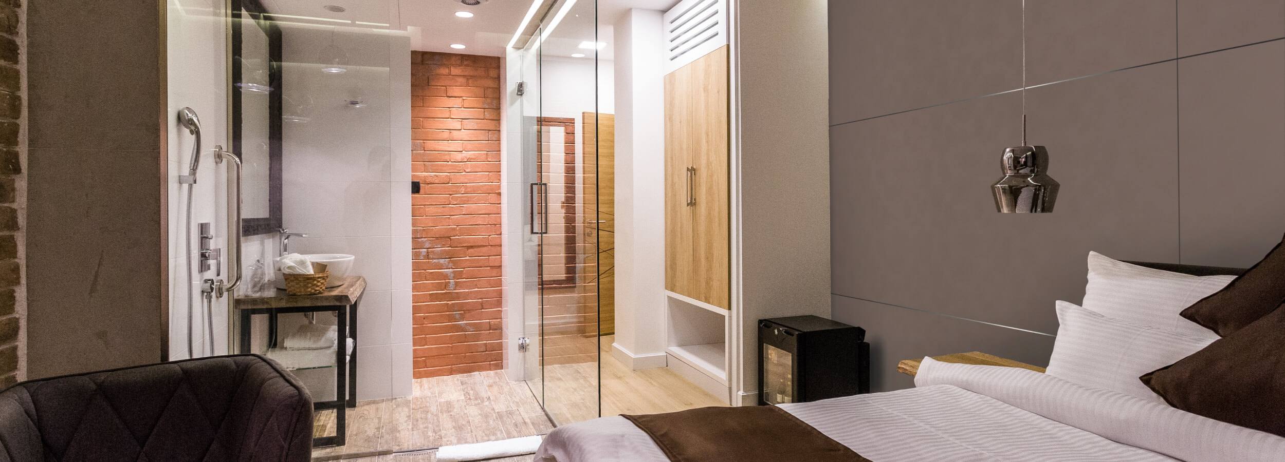 Habitación de hotel moderna con una pared de ladrillo, una ducha de vidrio y un panel de pared de cuero.