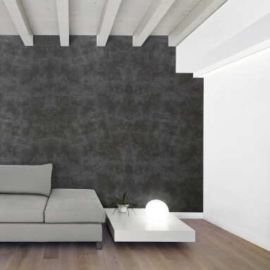 Vintage Wandpaneel imitiert Stein in einem modernen Interieur. Die strukturierte graue Wand bildet einen Kontrast zu den weißen Holzbalken der Decke und dem hellen Holzboden. Ein graues Sofa und ein weißer Couchtisch ergänzen das minimalistische Design.